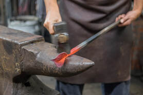 Picture blacksmith in leather apron hammers out the stem of a red-hot steel leaf on the horn of the anvil.