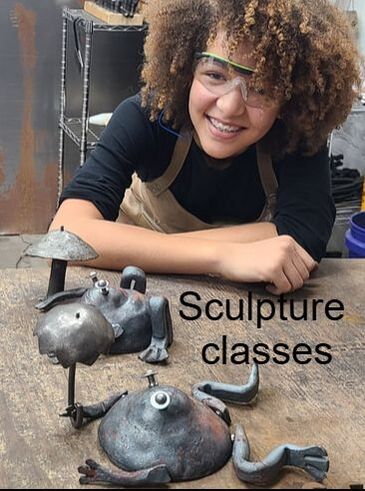A young student with safety glasses and an apron poses, smiling, beside her Frog (with umbrella) and Toad (with toadstool) sculptures. 